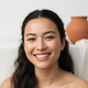 Close-up portrait of a smiling young woman with diverse features, looking directly at the camera. Soft, natural lighting and 